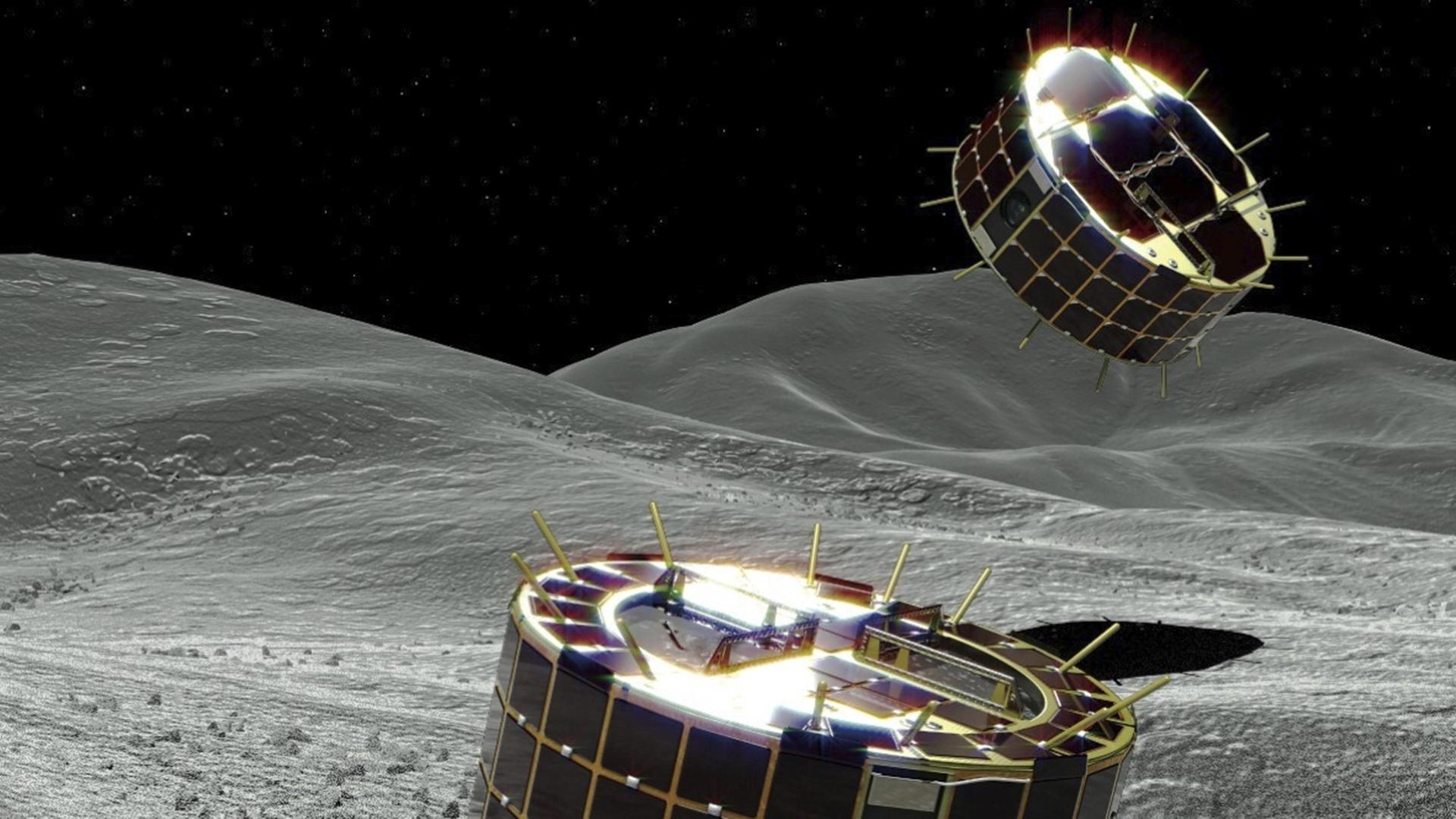 Die Computergrafik zeigt zwei zylinderförmigen und solarbetriebene Rover auf einem Asteroiden. Die Computergrafik zeigt zwei zylinderförmigen und solarbetriebene Rover auf einem Asteroiden.