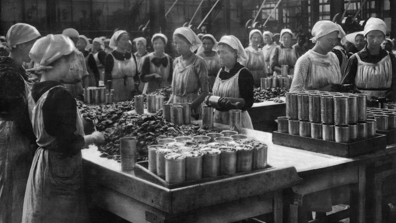 An einem Tisch stehen Frauen die Lebensmittel in Konserven verpacken. An einem Tisch stehen Frauen die Lebensmittel in Konserven verpacken.
