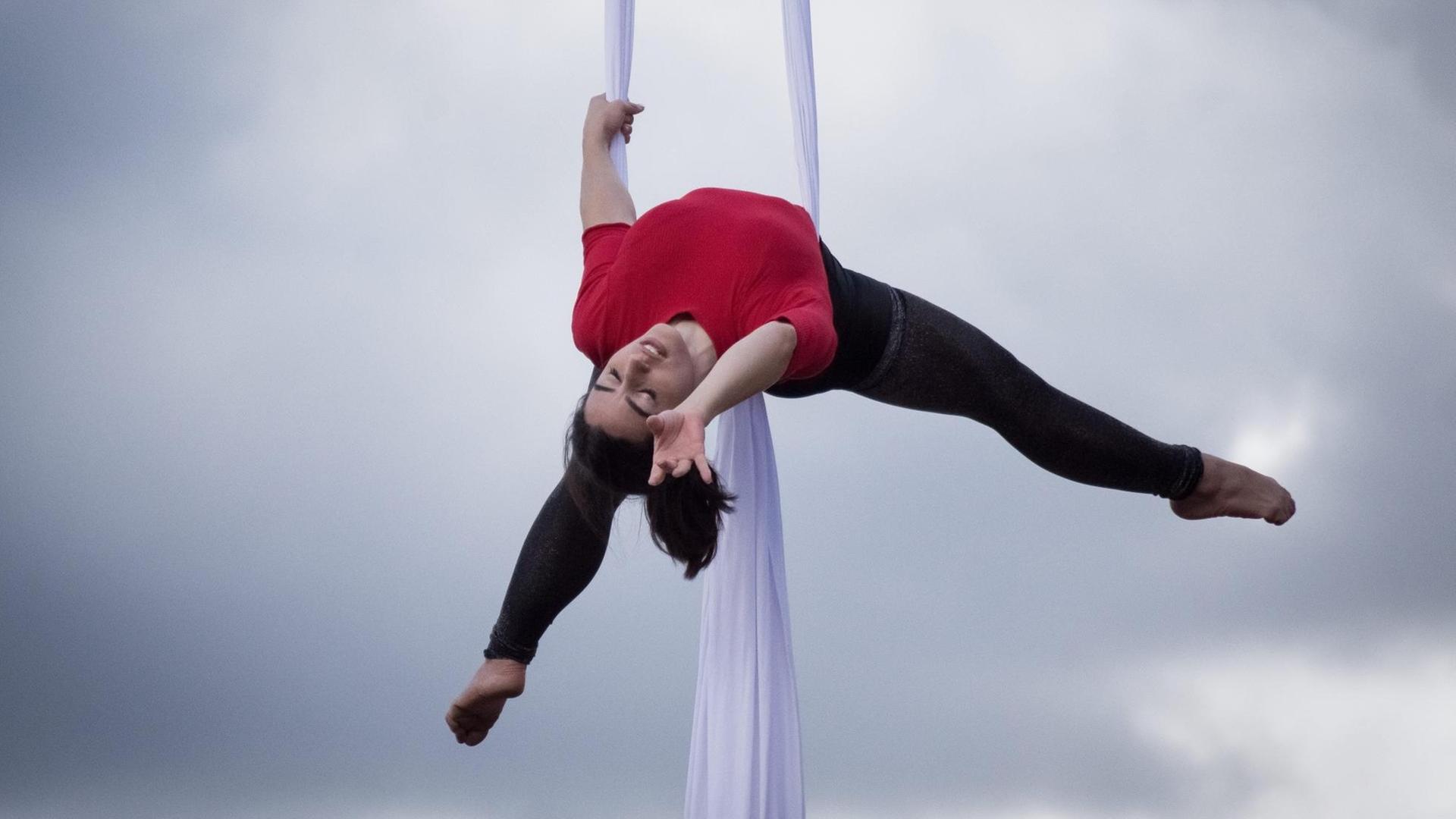 Eine Akrobatin schwebt an "Aerial Silks", zwei langen Vertikaltüchern, durch die Luft. Eine Akrobatin schwebt an "Aerial Silks", zwei langen Vertikaltüchern, durch die Luft.