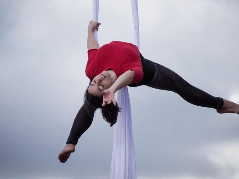 Eine Akrobatin schwebt an "Aerial Silks", zwei langen Vertikaltüchern, durch die Luft.