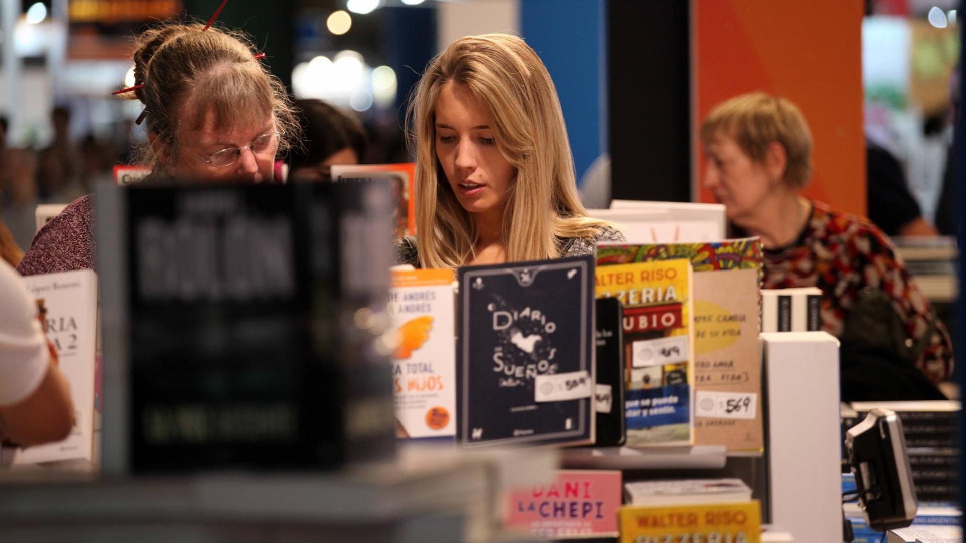 Zwei Frauen betrachten an einem Buchstand ein Buch während der Buchmesse in Buenos Aires 2019.