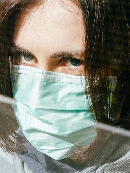Großaufnahme einer Frau mit Schutzmaske, die aus einem Fenster schaut.