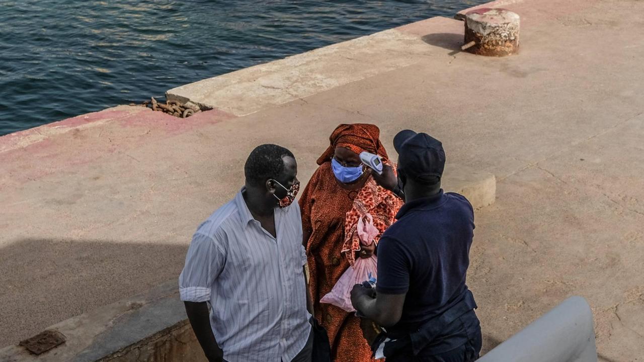 Zwei Passagiere in Dakar, Senegal, lassen ihre Temperatur prüfen, bevor sie an Bord eines Shuttlebootes steigen. 