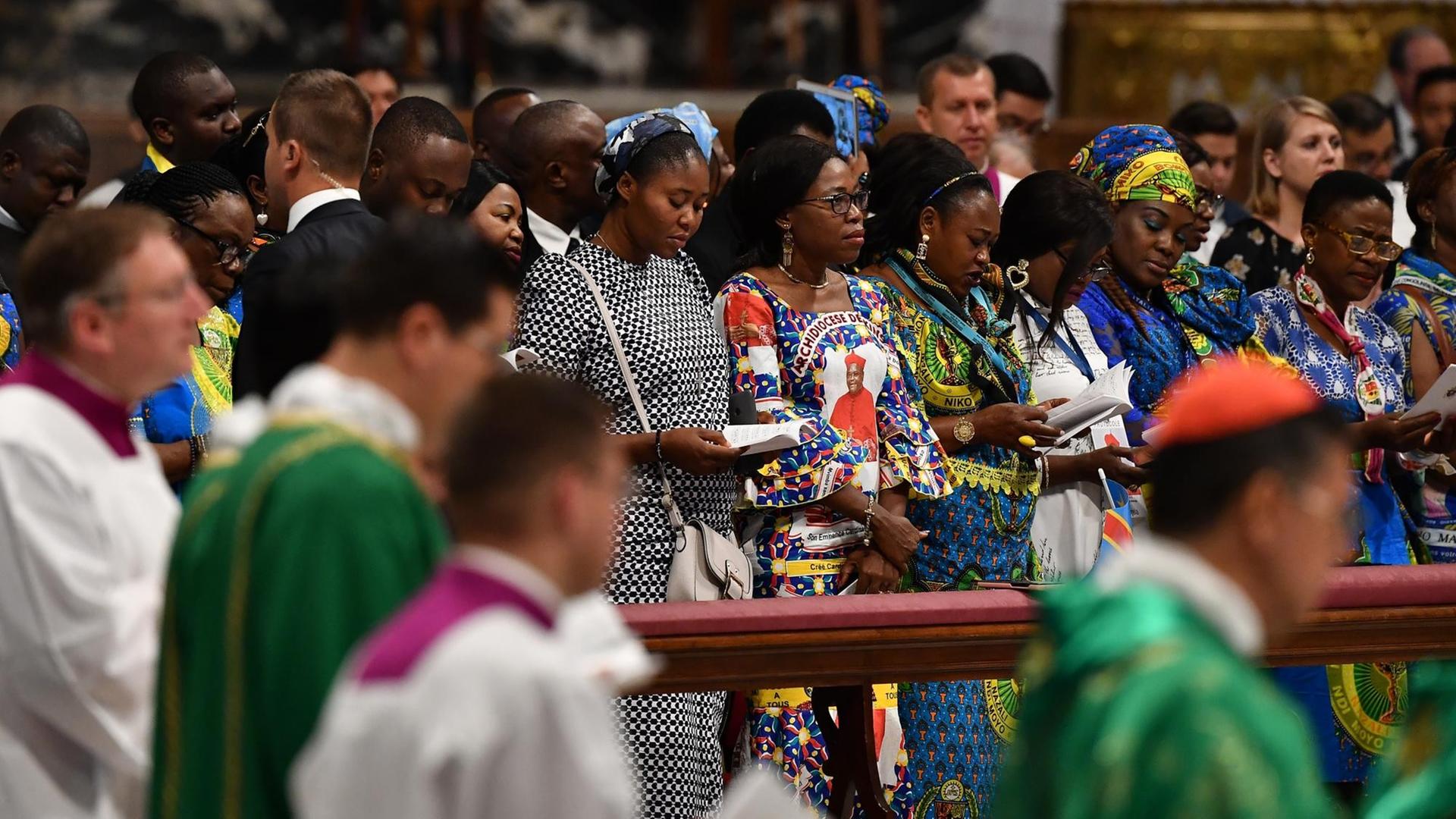 Frauen aus der Amazonas-Region stehen während der Messe in den Kirchenbänken. Daneben: Geistliche und Messdiener. Frauen aus der Amazonas-Region stehen während der Messe in den Kirchenbänken. Daneben: Geistliche und Messdiener.