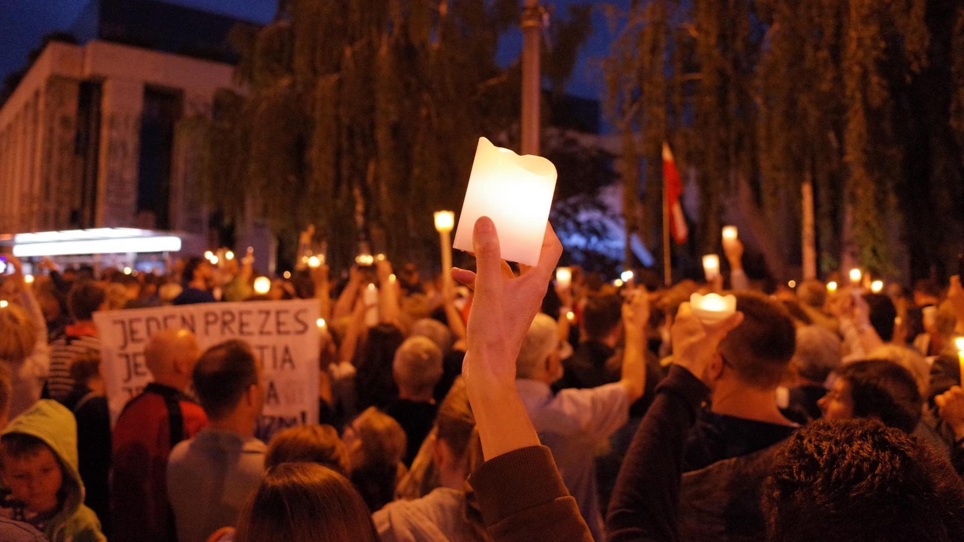 Demonstrationsgruppe bei Nacht, zentral hält jemand eine Kerze in die Höhe Demonstrationsgruppe bei Nacht, zentral hält jemand eine Kerze in die Höhe