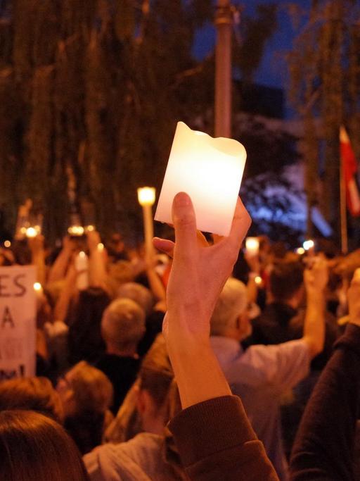 Demonstrationsgruppe bei Nacht, zentral hält jemand eine Kerze in die Höhe