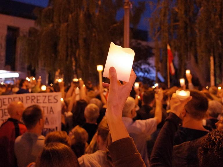 Demonstrationsgruppe bei Nacht, zentral hält jemand eine Kerze in die Höhe