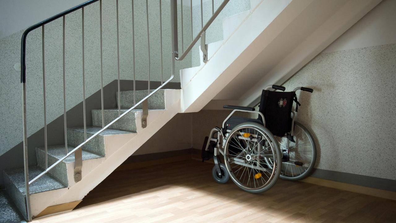 Ein Rollstuhl steht unter einer Treppe in einem Wohnhaus.
