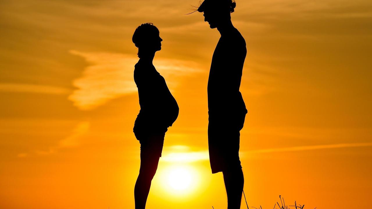 Werdende Eltern stehen auf einer Strohrolle im Sonnenuntergang. Werdende Eltern stehen auf einer Strohrolle im Sonnenuntergang.