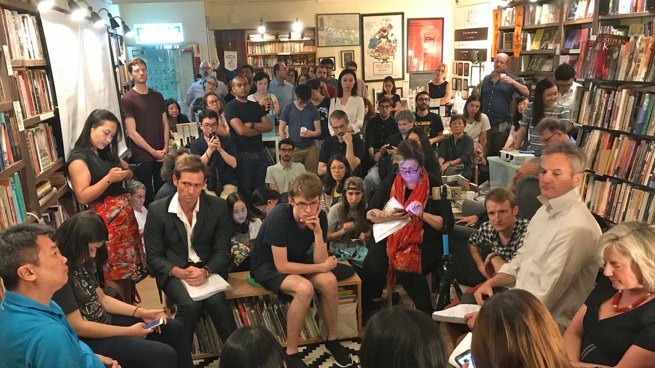 Blick auf die Zuhörer der Lesung von Tammy Ho in einer Buchhandlung. Die Zuschauer sitzen dichtgedrängt auf Stühlen, Tischen oder auf dem BOden. Viele haben SMartphones in der Hand. Die Wände sind mit Bücherregalen vollgestellt. Blick auf die Zuhörer der Lesung von Tammy Ho in einer Buchhandlung. Die Zuschauer sitzen dichtgedrängt auf Stühlen, Tischen oder auf dem BOden. Viele haben SMartphones in der Hand. Die Wände sind mit Bücherregalen vollgestellt.