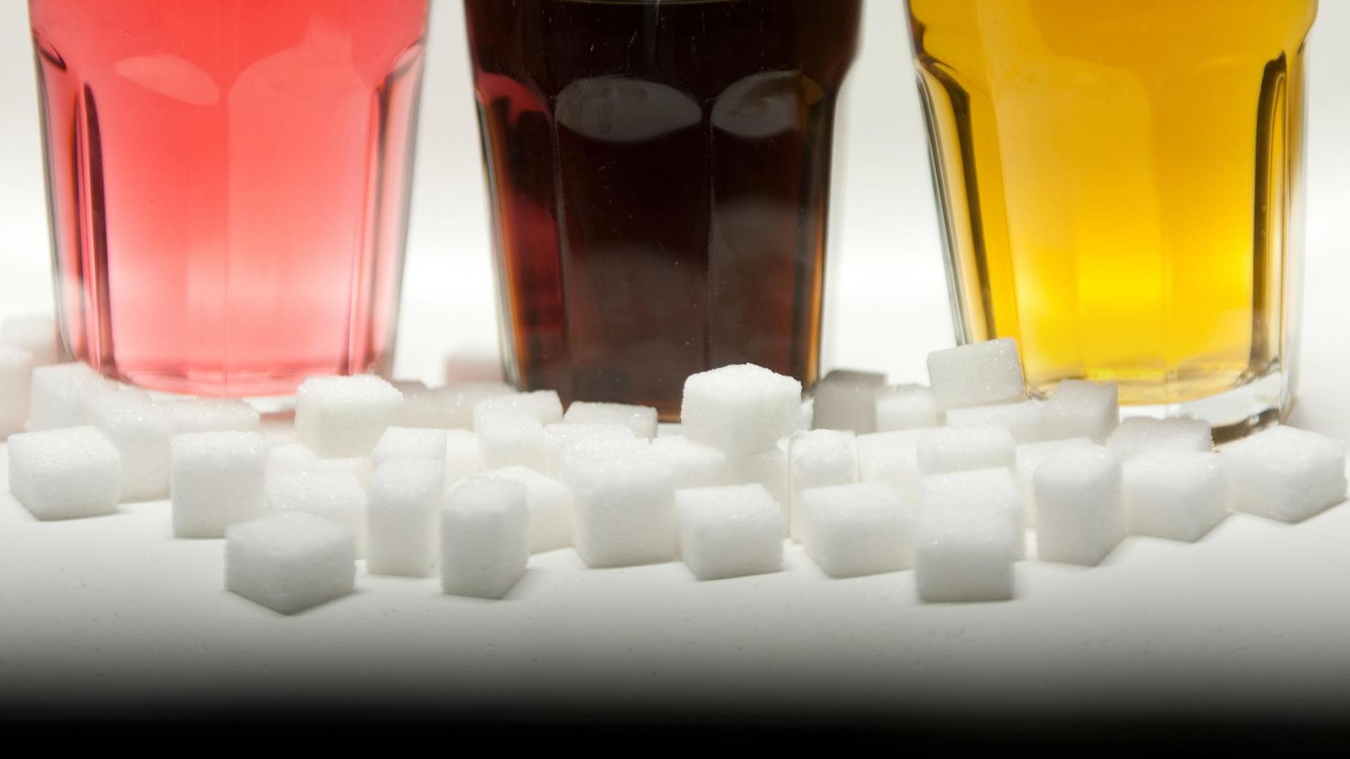 Drei Gläser gefüllt mit roter Limonade, Cola und Energy-Drink stehen am 23.08.2016 in Berlin neben Zuckerwürfeln auf einem Tisch.
