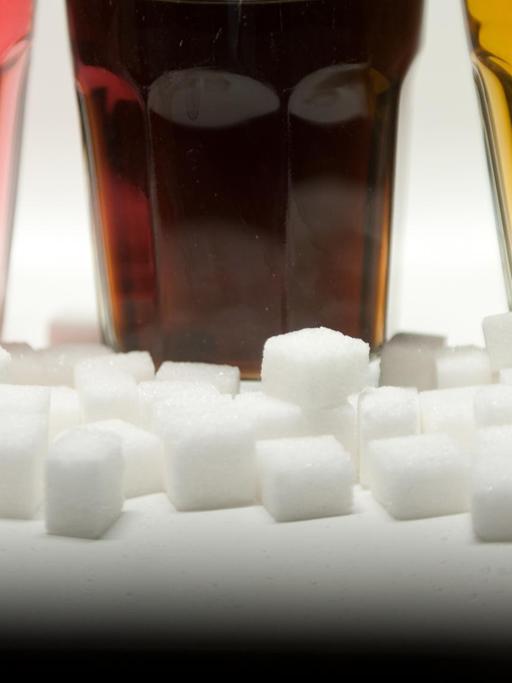 Drei Gläser gefüllt mit roter Limonade, Cola und Energy-Drink stehen am 23.08.2016 in Berlin neben Zuckerwürfeln auf einem Tisch.