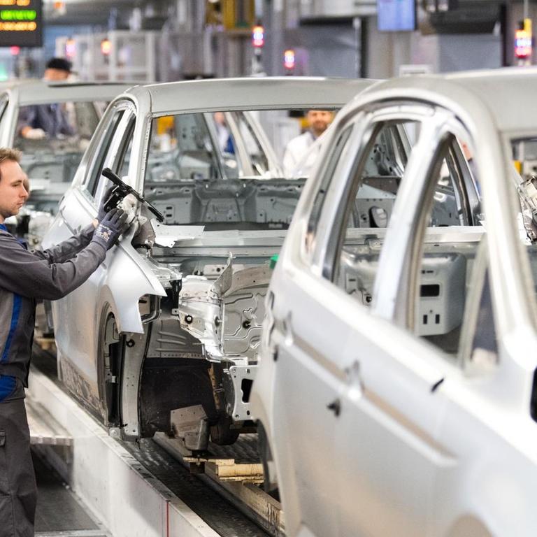 Das Bild zeigt einen Arbeiter an einem Montageband in einem VW-Werk. 