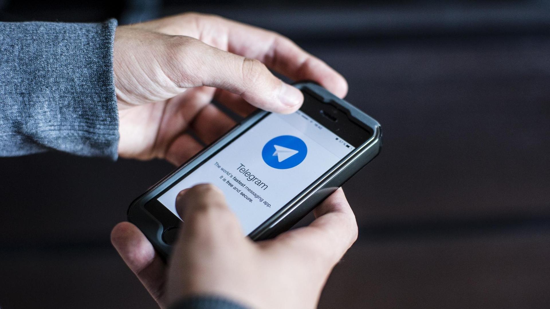 Zwei Hände halten ein Telefon auf dem der Messenger Telegram installiert ist. Zwei Hände halten ein Telefon auf dem der Messenger Telegram installiert ist.