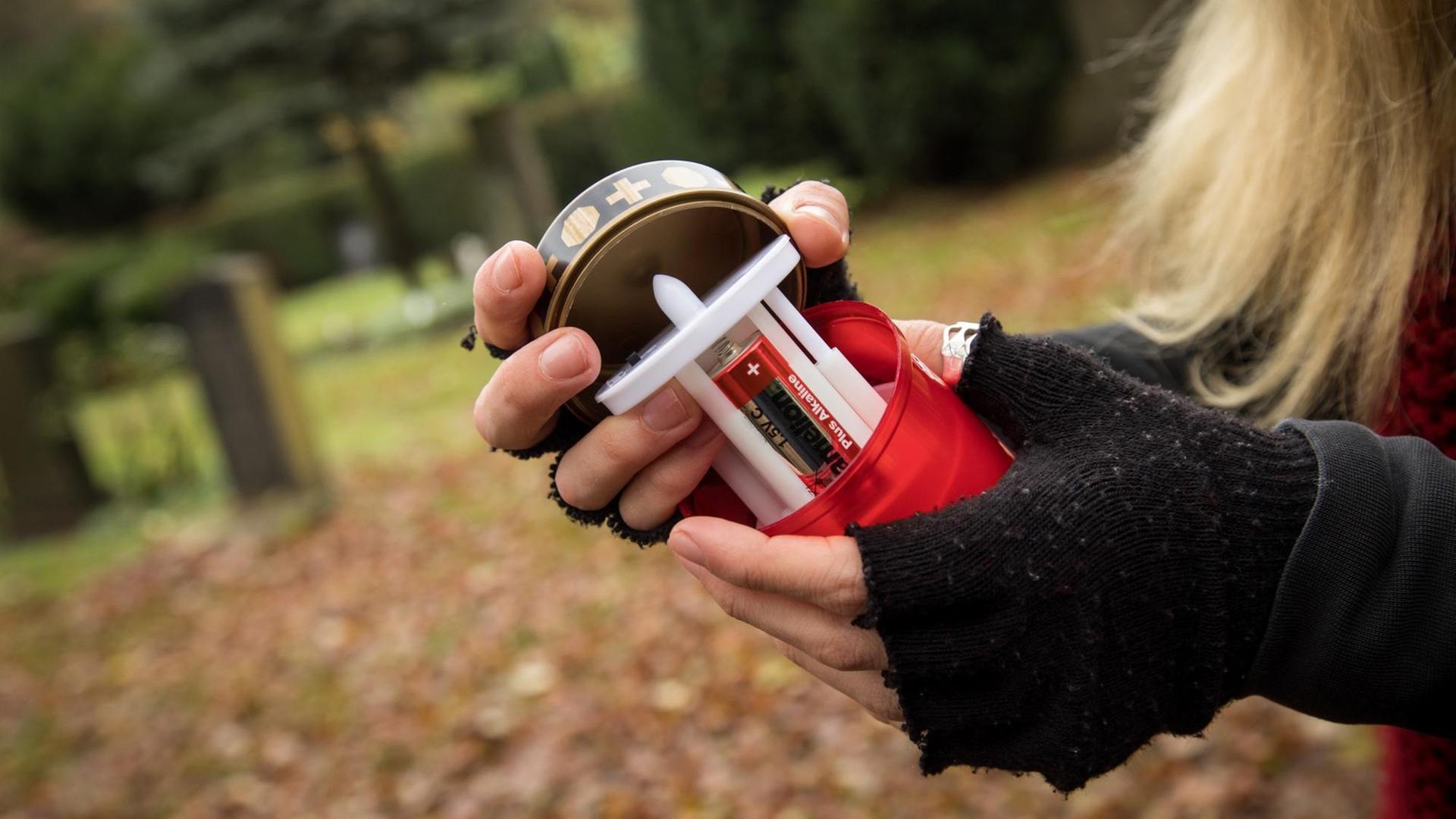 Eine Frau wechselt auf einem Friedhof die Batterien bei einer elekrischen Grabkerze aus. Eine Frau wechselt auf einem Friedhof die Batterien bei einer elekrischen Grabkerze aus.