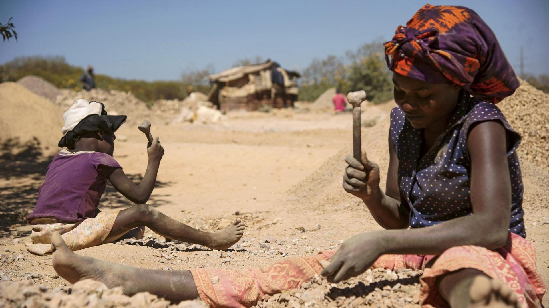 Ein Kind und eine Frau arbeiten in Lubumbashi in der Demokratischen Republik Kongo an Steinen aus einer Kobalt-Mine. Sie sitzen im Staub. Ein Kind und eine Frau arbeiten in Lubumbashi in der Demokratischen Republik Kongo an Steinen aus einer Kobalt-Mine. Sie sitzen im Staub.