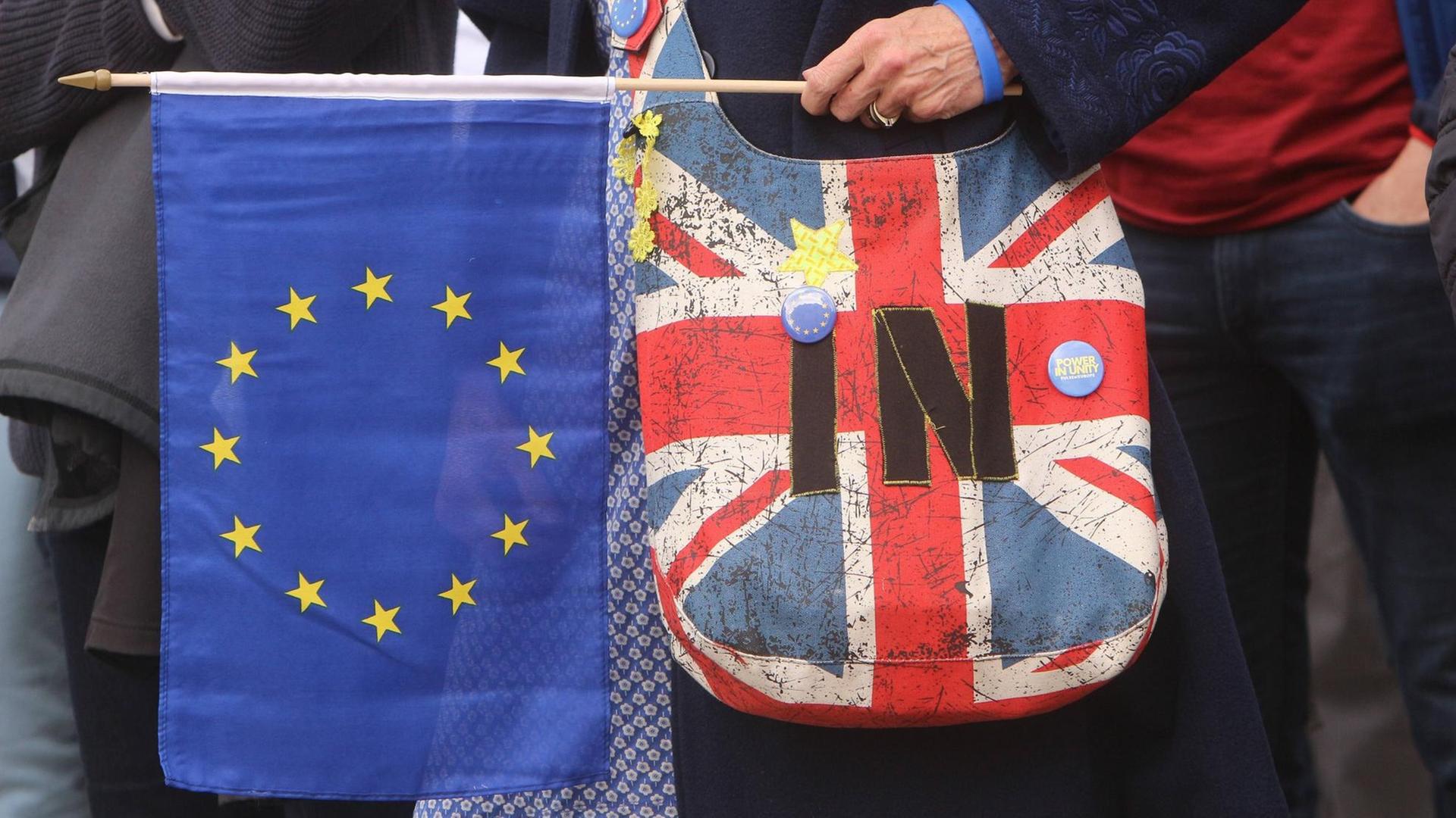 Frau mit einer Umhängetasche in den Farben der britischen Nationalflagge hält ein EU-Fähnchen Frau mit einer Umhängetasche in den Farben der britischen Nationalflagge hält ein EU-Fähnchen