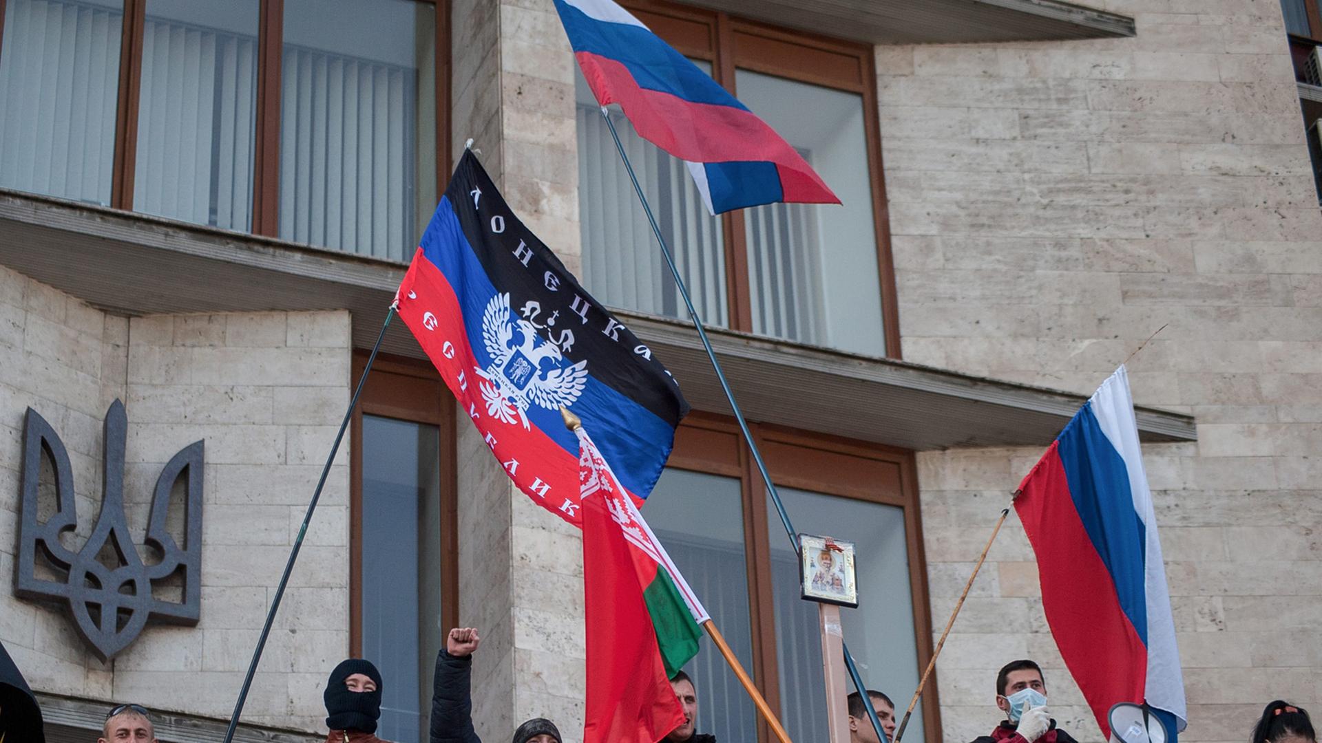 Vor einem Verwaltungsgebäude sind teils vermummte Demonstranten zu sehen, die die russische Flagge schwenken und skandieren. Vor einem Verwaltungsgebäude sind teils vermummte Demonstranten zu sehen, die die russische Flagge schwenken und skandieren.