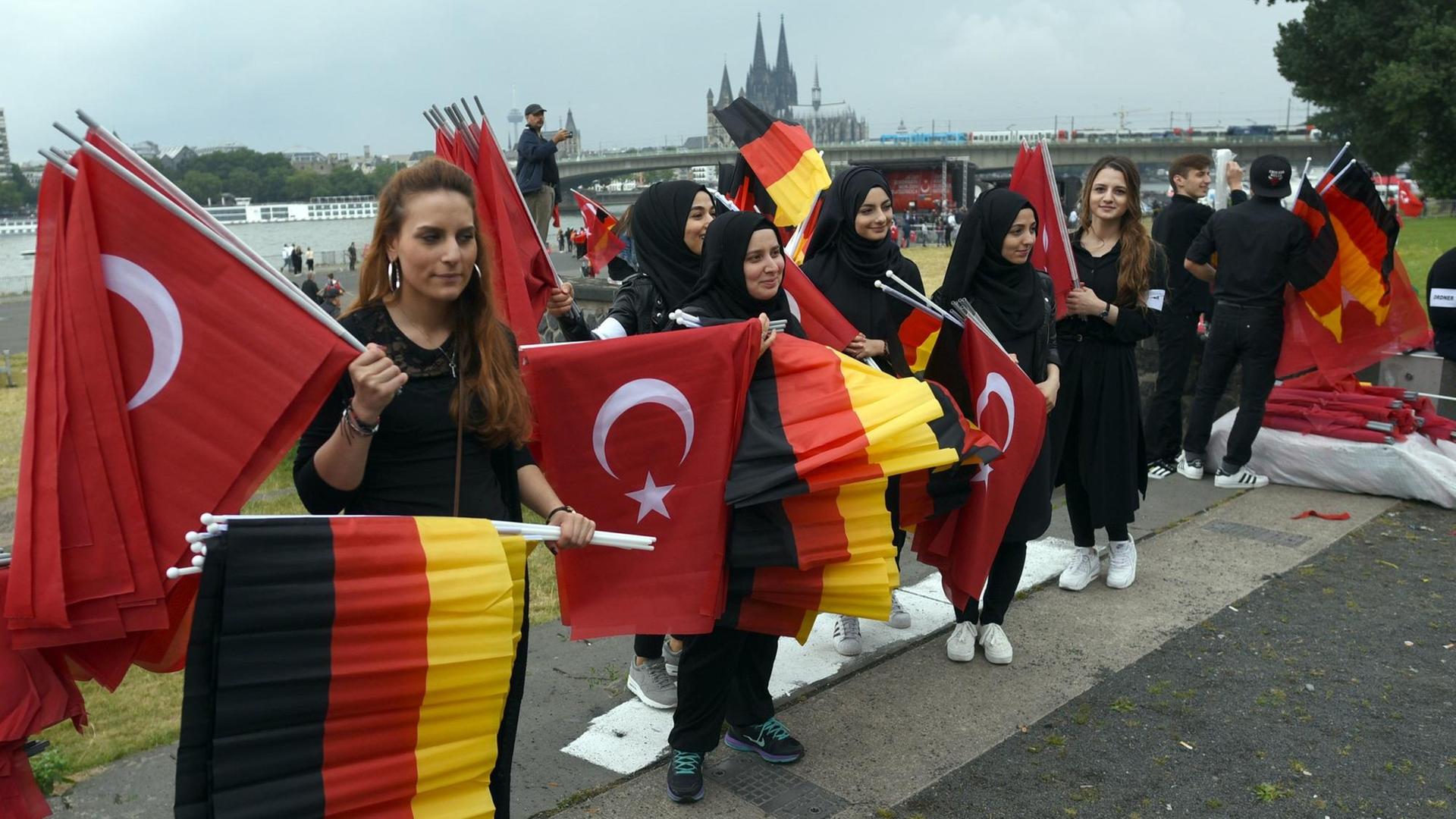 Türkische Frauen verteilen vor Beginn einer Kundgebung von Erdogan-Anhängern in Köln deutsche und türkische Fahnen. Türkische Frauen verteilen vor Beginn einer Kundgebung von Erdogan-Anhängern in Köln deutsche und türkische Fahnen.