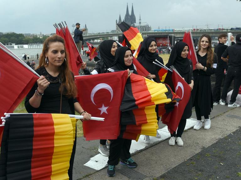 Türkische Frauen verteilen vor Beginn einer Kundgebung von Erdogan-Anhängern in Köln deutsche und türkische Fahnen.