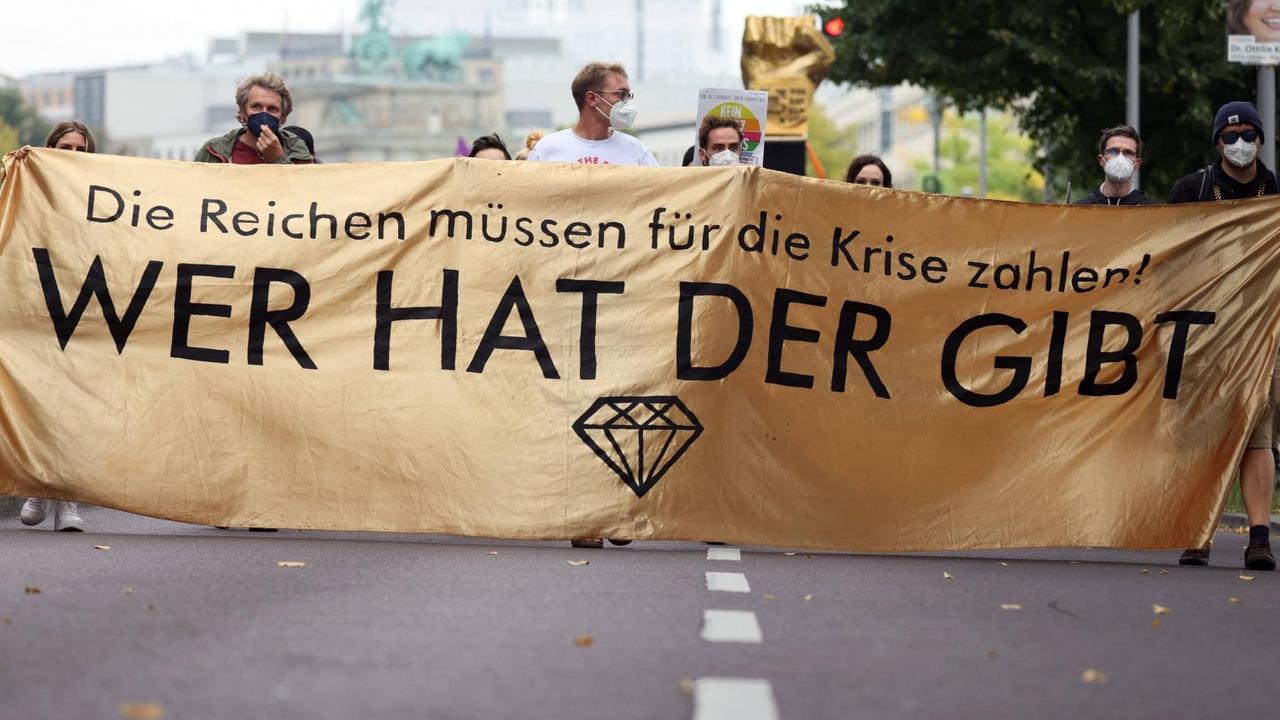 Menschen bei einer Demonstration. Sie tragen ein Banner auf dem geschrieben steht. "Die Reichen müssen für die Krise zahlen. Wer hat, der gibt." Menschen bei einer Demonstration. Sie tragen ein Banner auf dem geschrieben steht. "Die Reichen müssen für die Krise zahlen. Wer hat, der gibt."