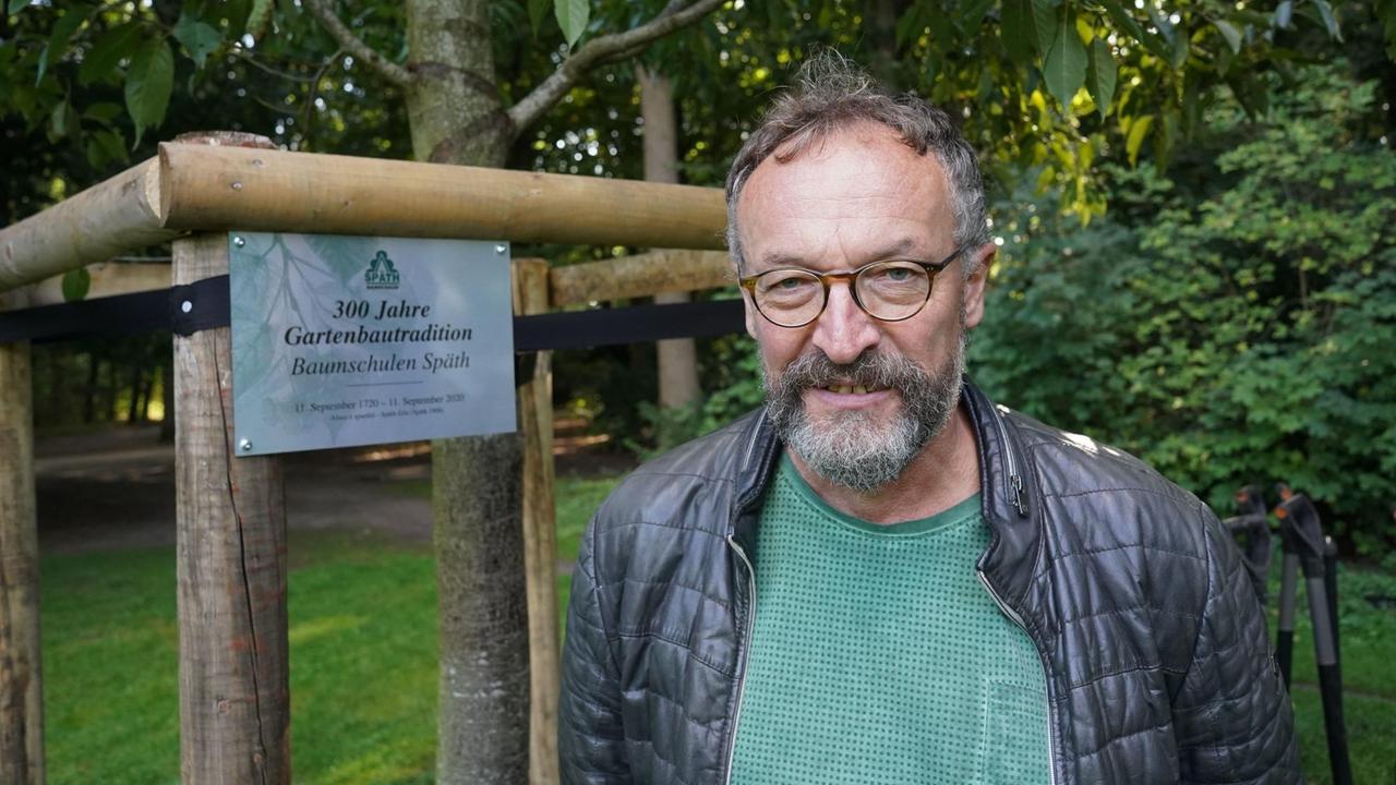 Porträt von Holger Zahn neben einem jungen Baum. Porträt von Holger Zahn neben einem jungen Baum.