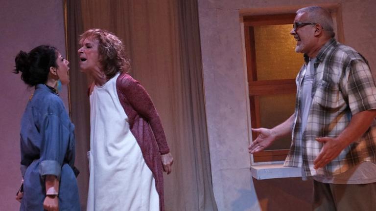 Auf einer Theaterbühne stehen zwei Frauen und ein Mann. Die Frauen streiten miteinander. Der Mann steht etwas abseits und streitet sich ebenfalls mit den Frauen. Auf einer Theaterbühne stehen zwei Frauen und ein Mann. Die Frauen streiten miteinander. Der Mann steht etwas abseits und streitet sich ebenfalls mit den Frauen.