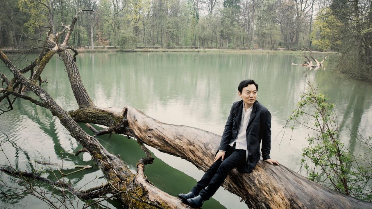 William Youn sitzt auf einem Baumstamm, der quer in einen See ragt