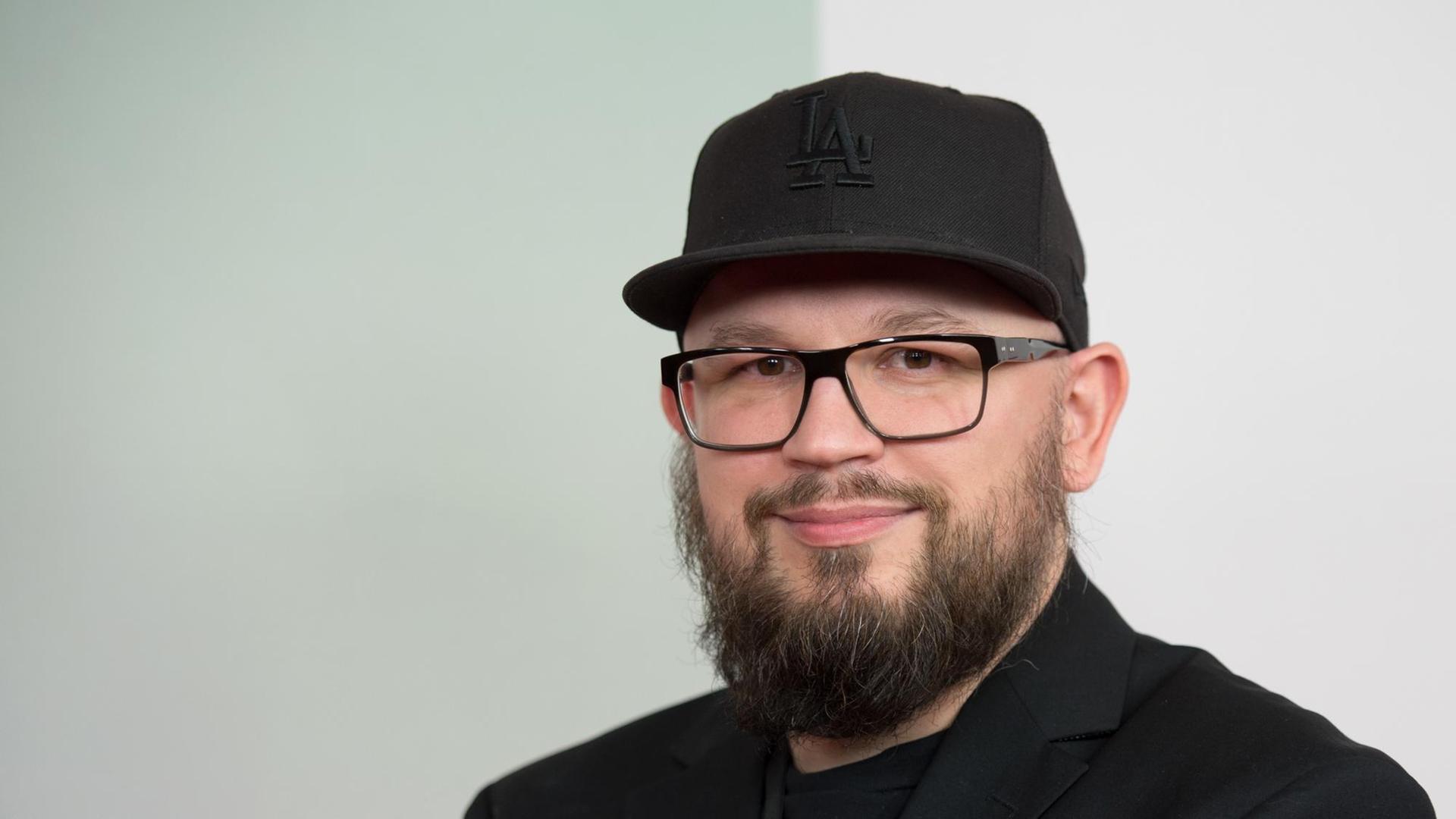 Christian Alvert trägt ein schwarzes Shirt, ein schwarzes Sakko und eine schwarze Mütze Christian Alvert trägt ein schwarzes Shirt, ein schwarzes Sakko und eine schwarze Mütze