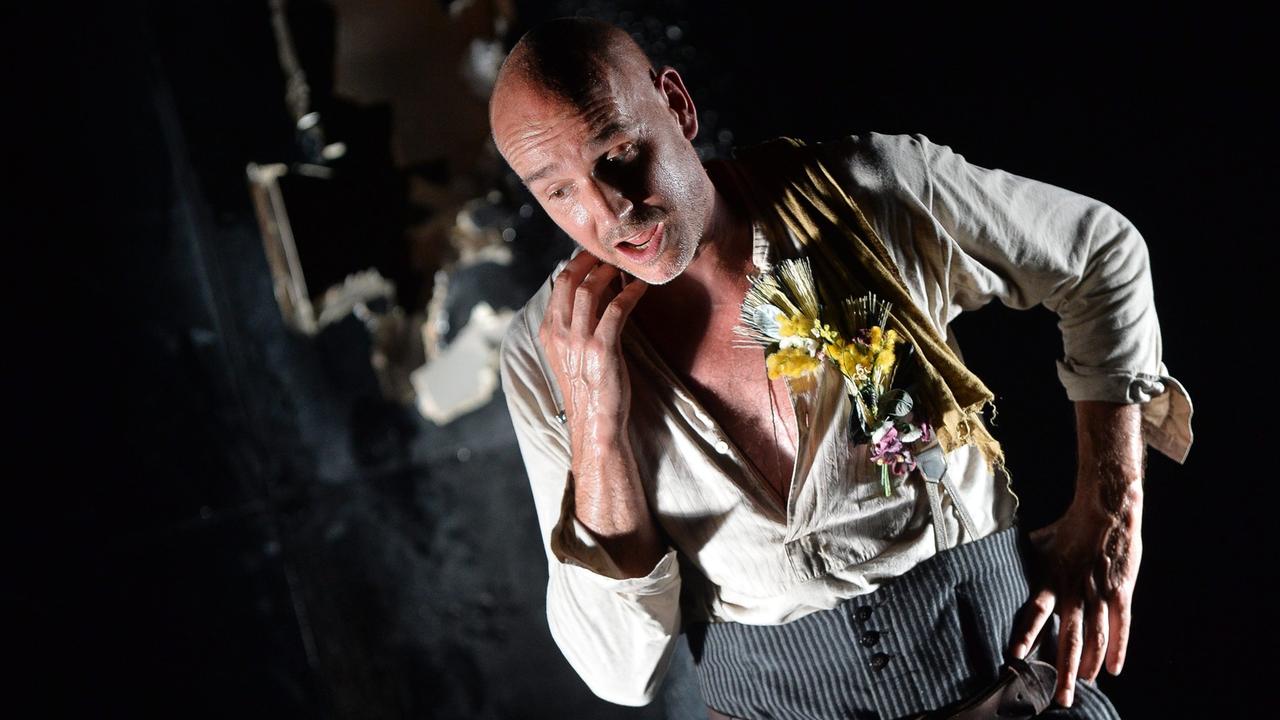 Paul Herwig als Georg Trakl in "Der Abschied", Schauspieler mit Glatze, hellem aufgerissenen Hemd und grauer Hose auf einer dunklen Bühne Paul Herwig als Georg Trakl in "Der Abschied", Schauspieler mit Glatze, hellem aufgerissenen Hemd und grauer Hose auf einer dunklen Bühne