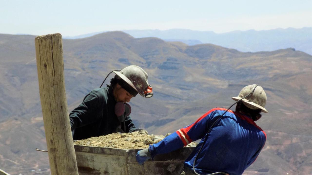 Zwei Minenarabeiter mit schwerem Karren an am Cerro Rico, im Hintergrund liegt Potosí.