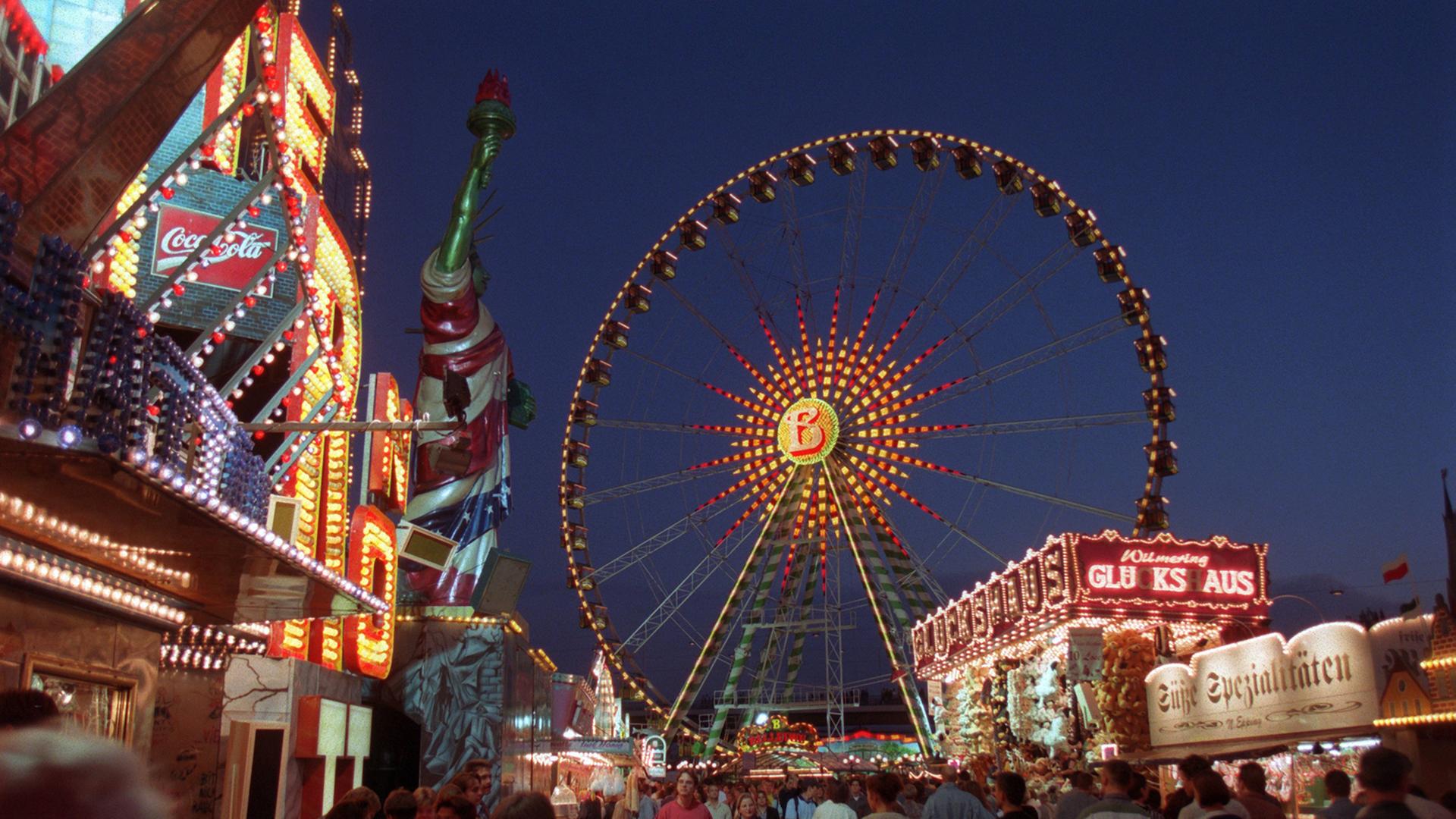 Eine bunt beleuchtete Kirmes mit einem Riesenrad in den Abendstunden. Eine bunt beleuchtete Kirmes mit einem Riesenrad in den Abendstunden.