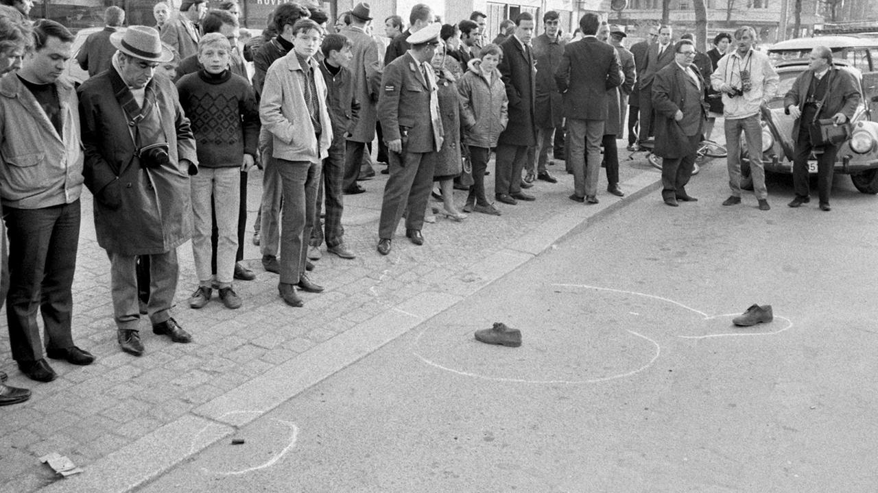 Passanten schauen auf die Schuhe von Rudi Dutschke, die noch am Tatort liegen. Dutschke wurde am 11. April 1968 vor der Geschäftsstelle des SDS am Kurfürstendamm niedergeschossen und lebensgefährlich verletzt. Passanten schauen auf die Schuhe von Rudi Dutschke, die noch am Tatort liegen. Dutschke wurde am 11. April 1968 vor der Geschäftsstelle des SDS am Kurfürstendamm niedergeschossen und lebensgefährlich verletzt.