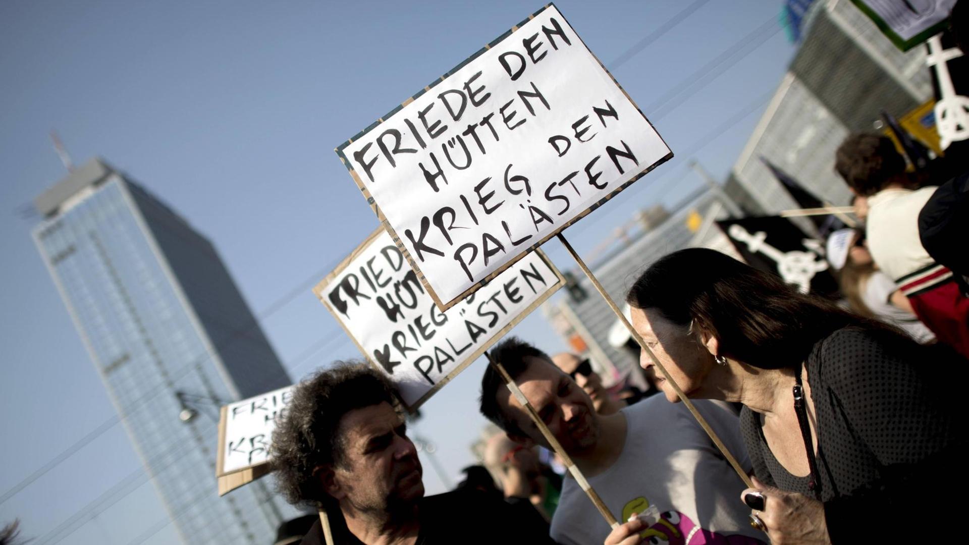 Drei Menschen stehen bei der Mietendemo in Berlin zusammen und halten ein Schilder mit der Aufschrift "Friede Den Hütten - Krieg Den Palästen". Drei Menschen stehen bei der Mietendemo in Berlin zusammen und halten ein Schilder mit der Aufschrift "Friede Den Hütten - Krieg Den Palästen".
