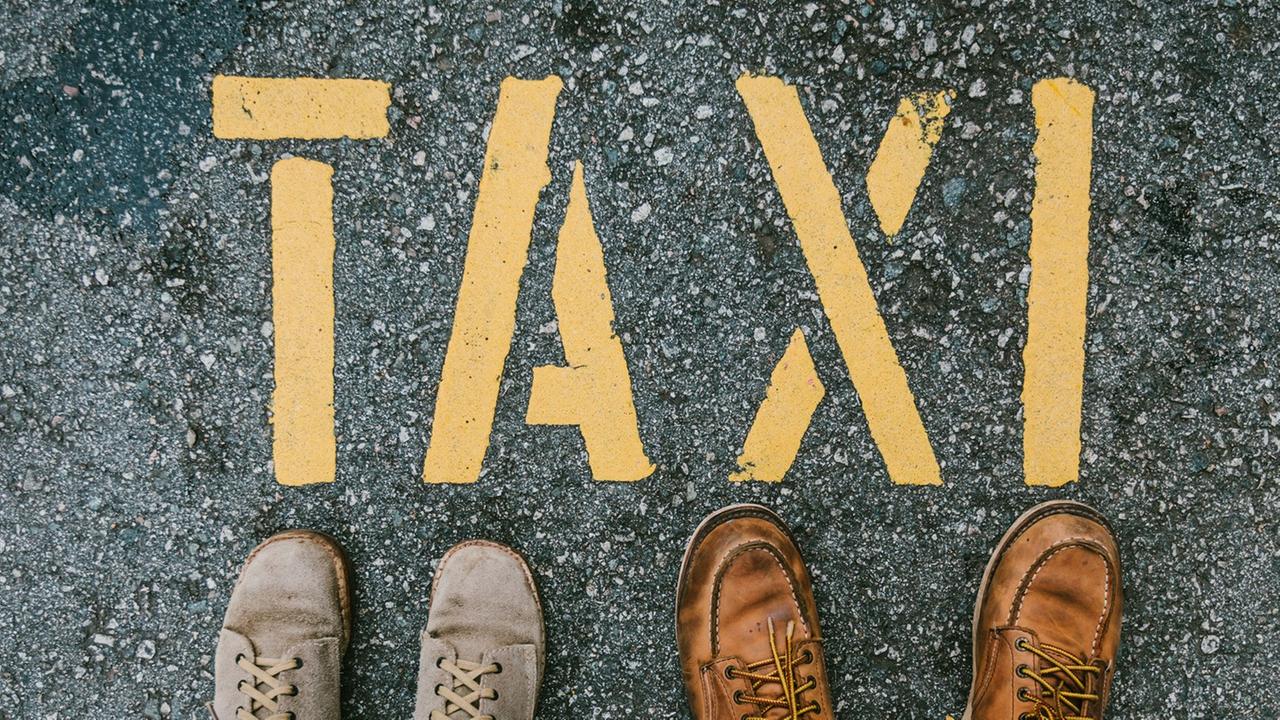 Zwei Menschen stehen vor einem Taxi-Schriftzug auf der Straße Zwei Menschen stehen vor einem Taxi-Schriftzug auf der Straße