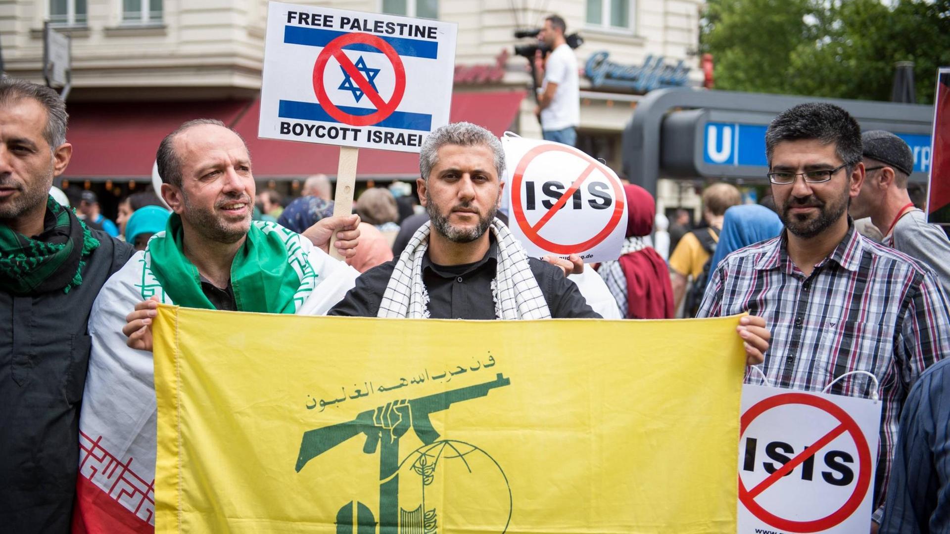 Ein Demonstrationsteilnehmer haelt die gelb-gruene Fahne der islamistischen Hisbollah-Partei und seine Mitdemonstranten haben Schilder gegen die Terrororganisation Islamischer Staat, IS. Ein Demonstrationsteilnehmer haelt die gelb-gruene Fahne der islamistischen Hisbollah-Partei und seine Mitdemonstranten haben Schilder gegen die Terrororganisation Islamischer Staat, IS.