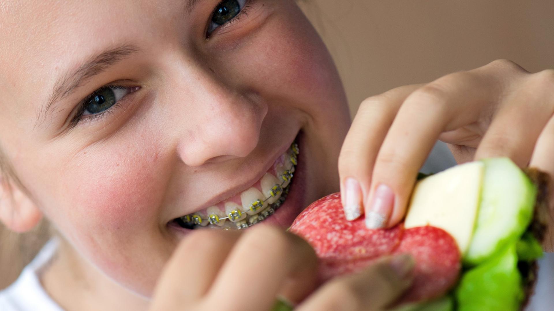 Ein Mädchen mit Zahnspange hält ein selbst belegtes Butterbrot in den Händen.