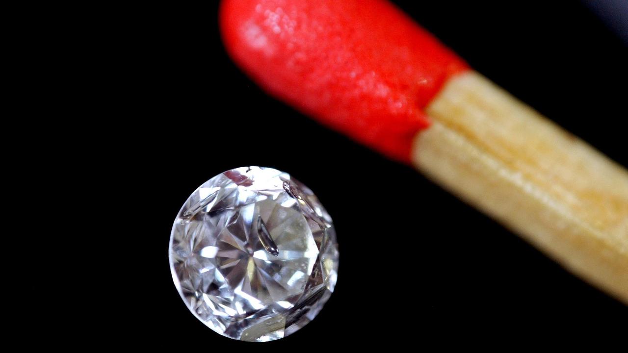 Ein roter Streichholzkopf neben einem Diamanten auf schwarzem Filz.