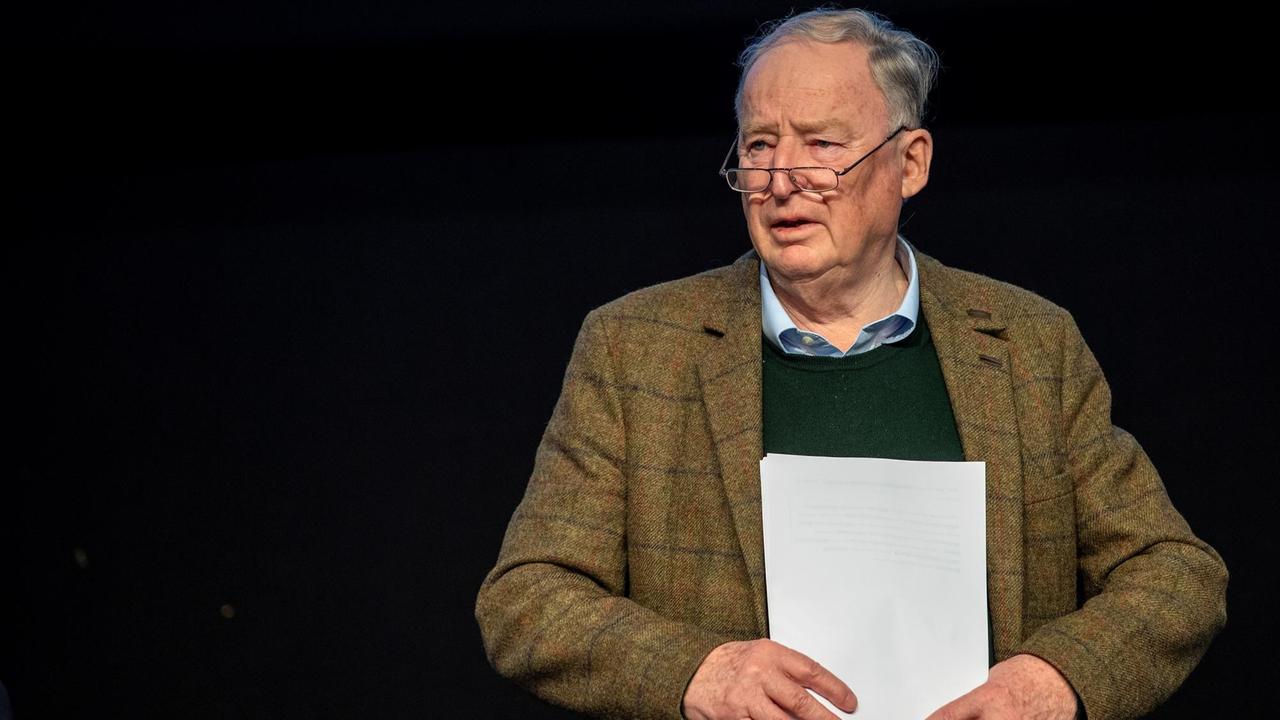 Gauland mit braunkariertem Jackett vor einem schwarzen Hintergrund. Er hält das Redemanuskript vor sich. 