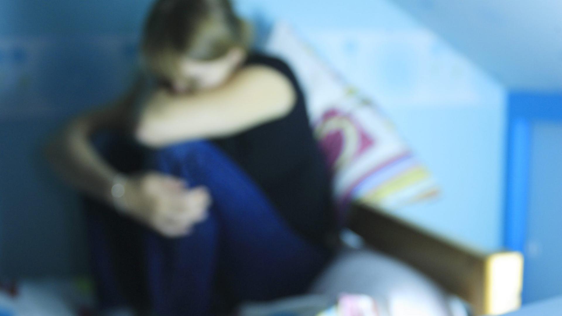 Eine verzweifelte junge Frau hockt auf einem Bett. Im Vordergrund: Tabletten. Eine verzweifelte junge Frau hockt auf einem Bett. Im Vordergrund: Tabletten.