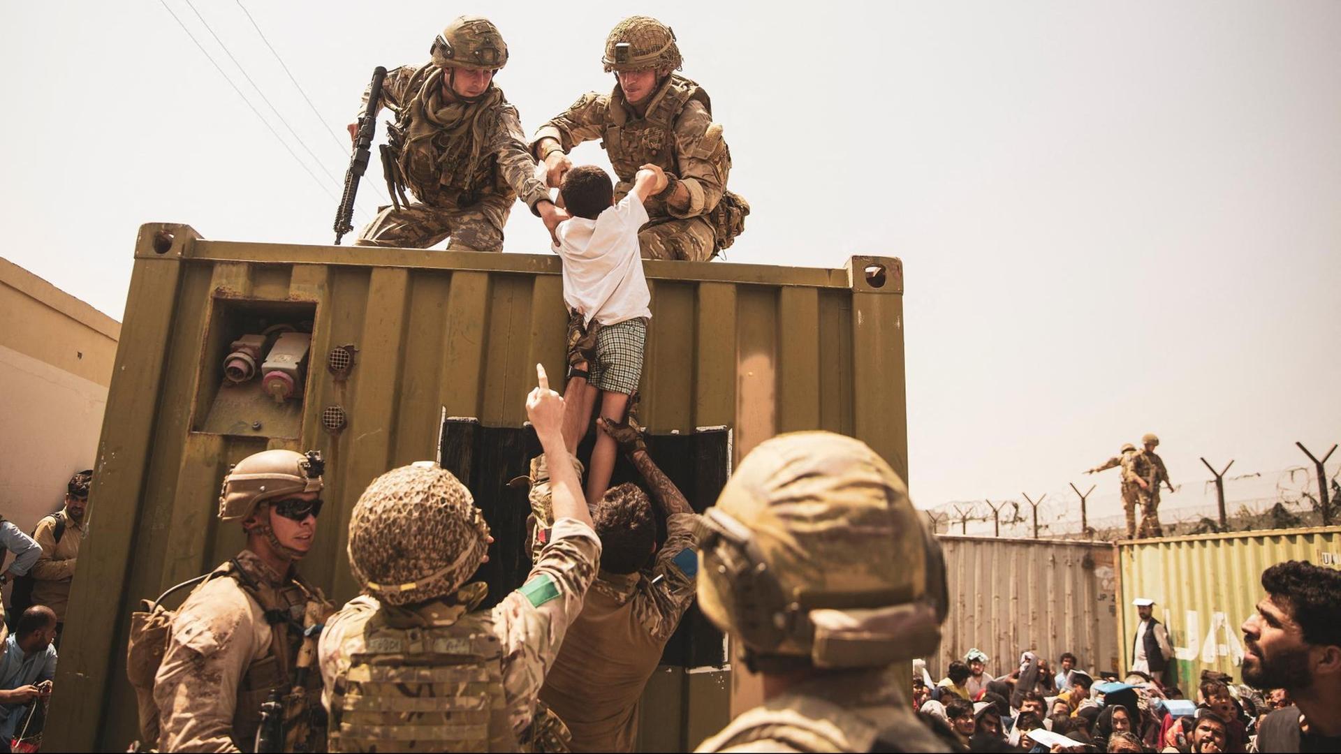 Britische Koalitionstruppen, türkische Koalitionstruppen und US-Marines helfen einem Kind während einer Evakuierung am internationalen Flughafen Hamid Karzai in Kabul. Britische Koalitionstruppen, türkische Koalitionstruppen und US-Marines helfen einem Kind während einer Evakuierung am internationalen Flughafen Hamid Karzai in Kabul.