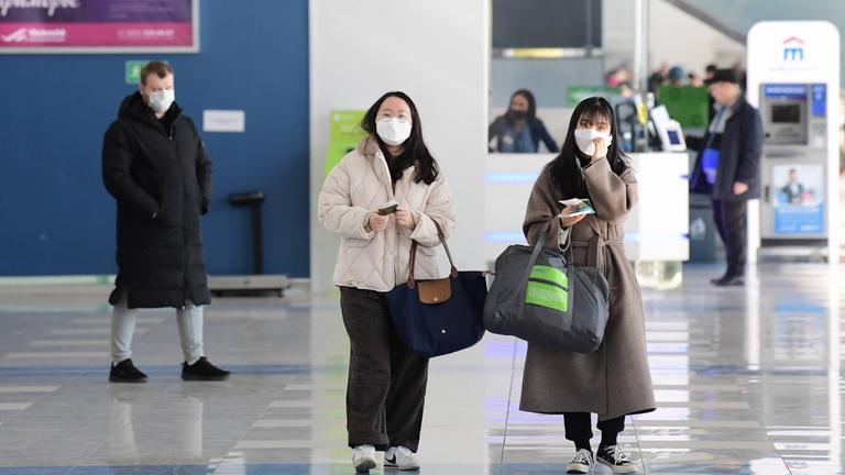 Menschen mit Schutzmasken laufen in einem Flughafen.