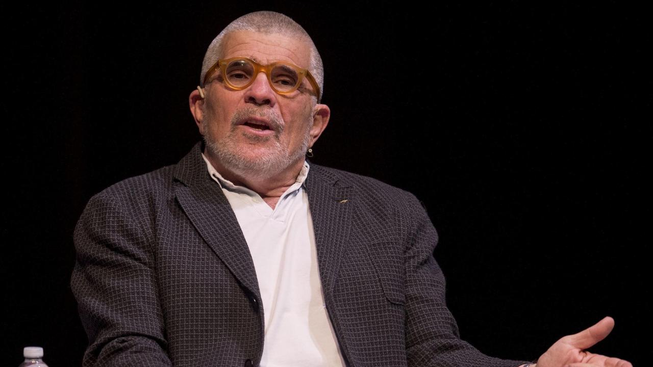 Der Dramatiker David Mamet, 2018 bei einer Podiumsdiskussion in Los Angeles. Mamet hat graues Haar und trägt über seinem weißen Hemd ein Sakko. Er sitzt auf einem Stuhl. Der Dramatiker David Mamet, 2018 bei einer Podiumsdiskussion in Los Angeles. Mamet hat graues Haar und trägt über seinem weißen Hemd ein Sakko. Er sitzt auf einem Stuhl.