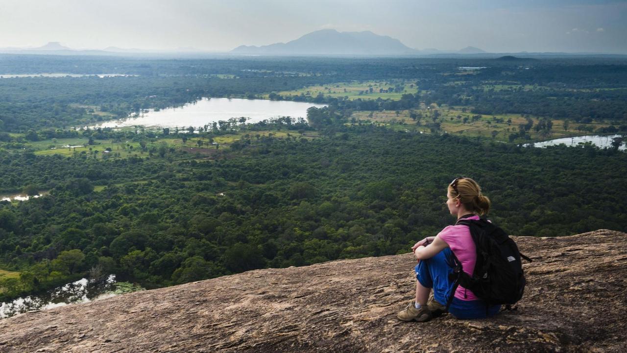 Eine Frau sitzt auf dem Pidurangala Felsen in Sri Lanka.
