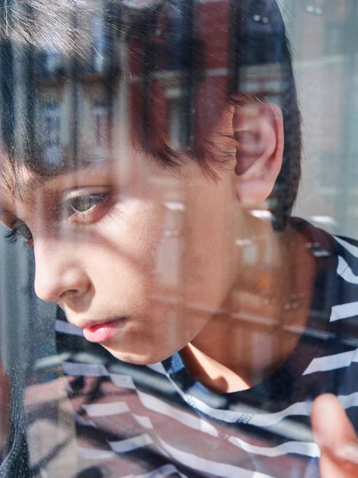 Ein Junge schaut unglücklich aus dem Fenster. (Symbolfoto)