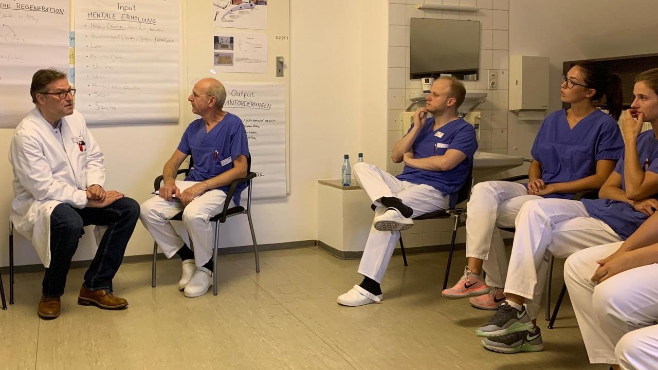 Wolfgang E. Thasler sitzt in einem weißen Kittel vor beschriebenen Blättern. Neben ihn sitzt ein Kollege. Auf der rechten Seite sitzen noch mehr Medizinier mit blauen Oberteilen und weißen Hosen. Wolfgang E. Thasler sitzt in einem weißen Kittel vor beschriebenen Blättern. Neben ihn sitzt ein Kollege. Auf der rechten Seite sitzen noch mehr Medizinier mit blauen Oberteilen und weißen Hosen.