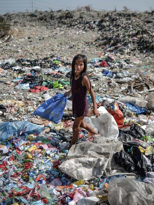 Ein Mädchen läuft mit einer Plastiktüte in der Hand über eine Müllhalde auf den Philippinen