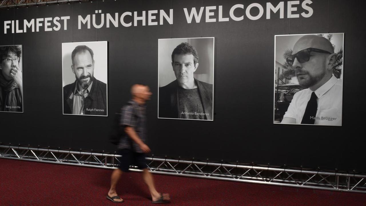 Ein Besucher geht im Festivalgebäude des Gasteig über einen roten Teppich vor Plakaten von Bong Joon Ho (l-r), Ralph Fiennes, Antonio Banderas und Mads Brügger. Ein Besucher geht im Festivalgebäude des Gasteig über einen roten Teppich vor Plakaten von Bong Joon Ho (l-r), Ralph Fiennes, Antonio Banderas und Mads Brügger.