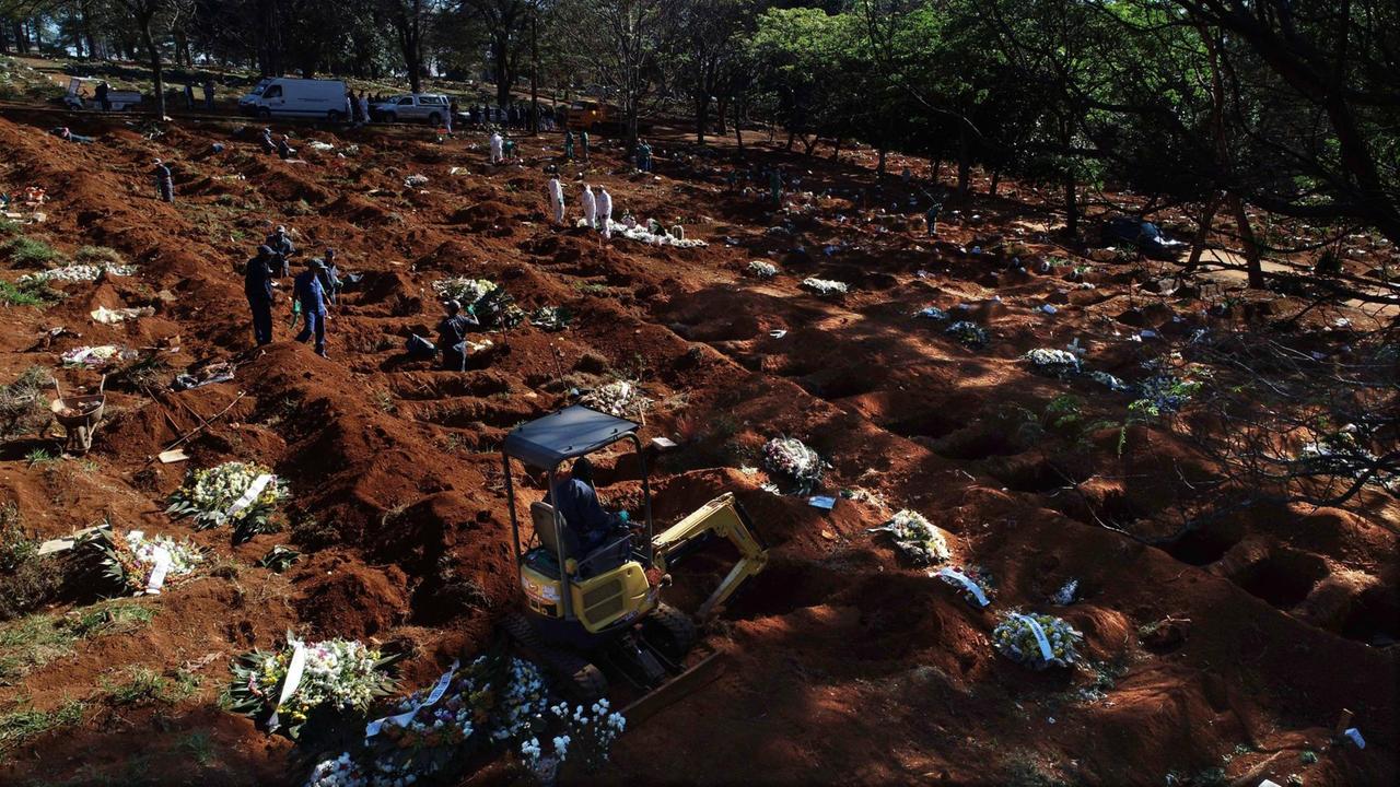 Luftaufnahme einer Drohne. Auf einem Feld sind zahlreiche Gräber für Coronaopfer ausgehoben worden. Auf einzelnen Gräbern liegen Kränze. 