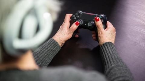 Eine Seniorin hält den Controller einer Playstation in den Händen.